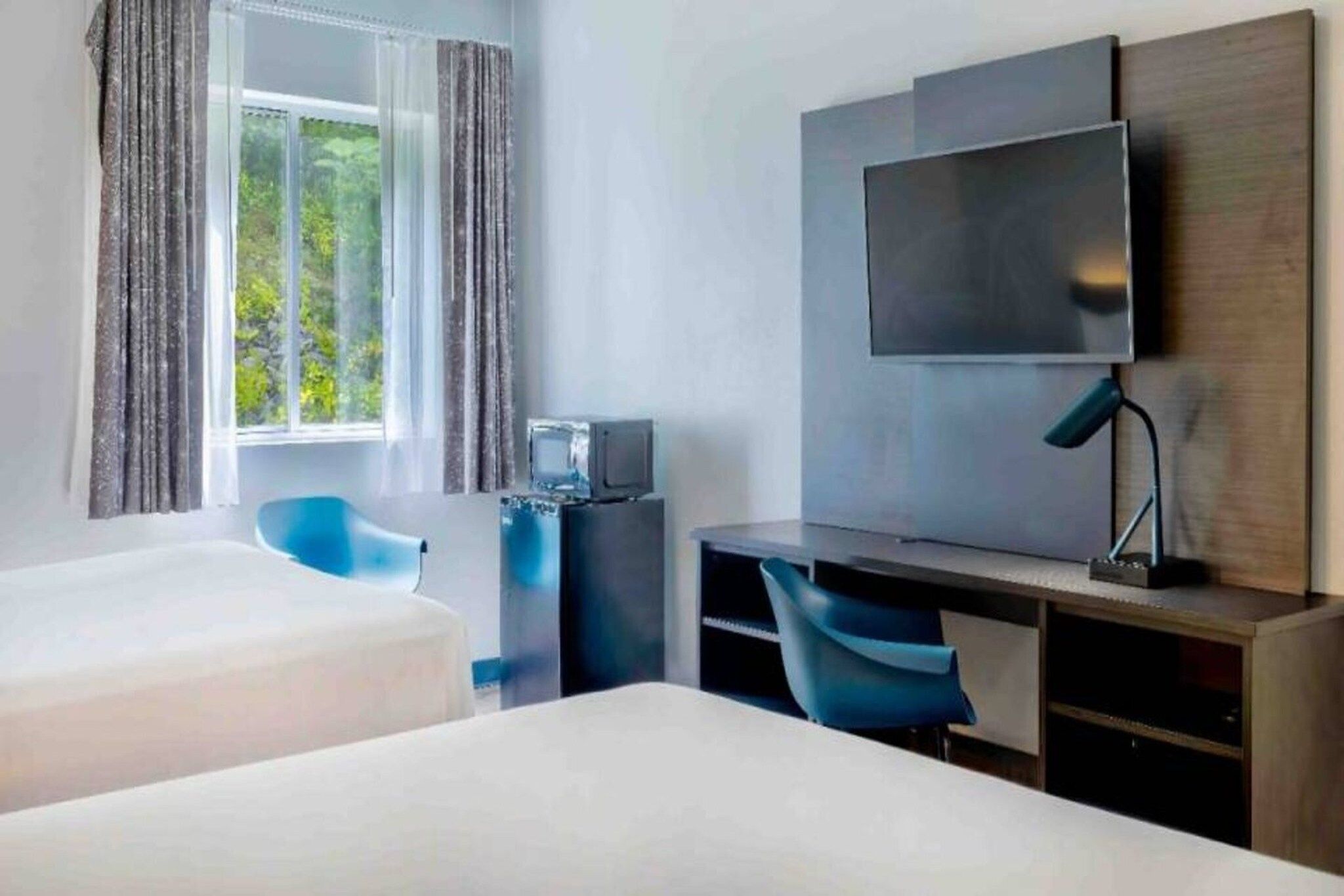 Ett hotellrum med två sängar, ett skrivbord, en stol, en tv och ett fönster med gardiner.