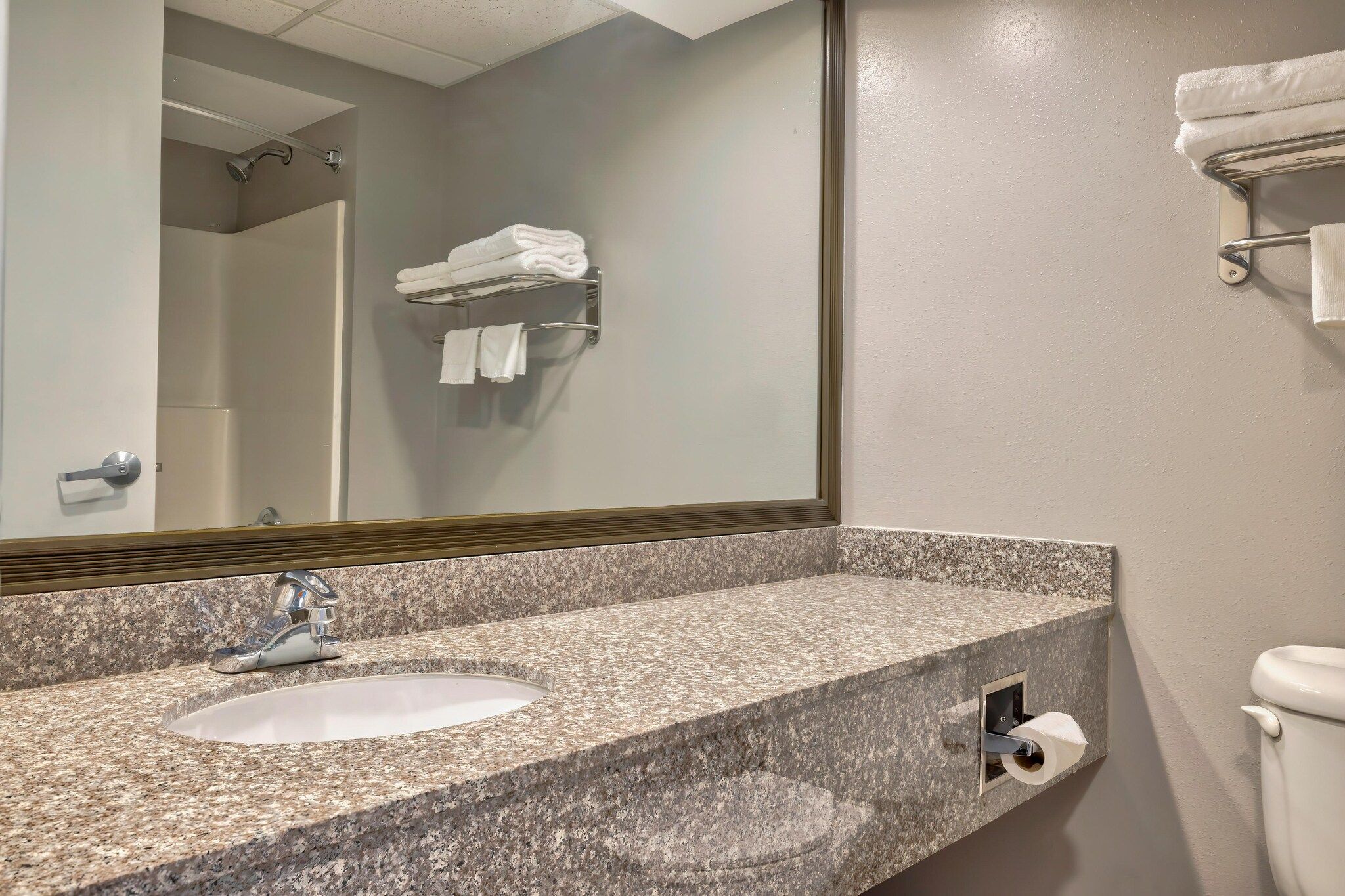 A bathroom with a granite countertop, a sink, a mirror, a towel rack, and a toilet.