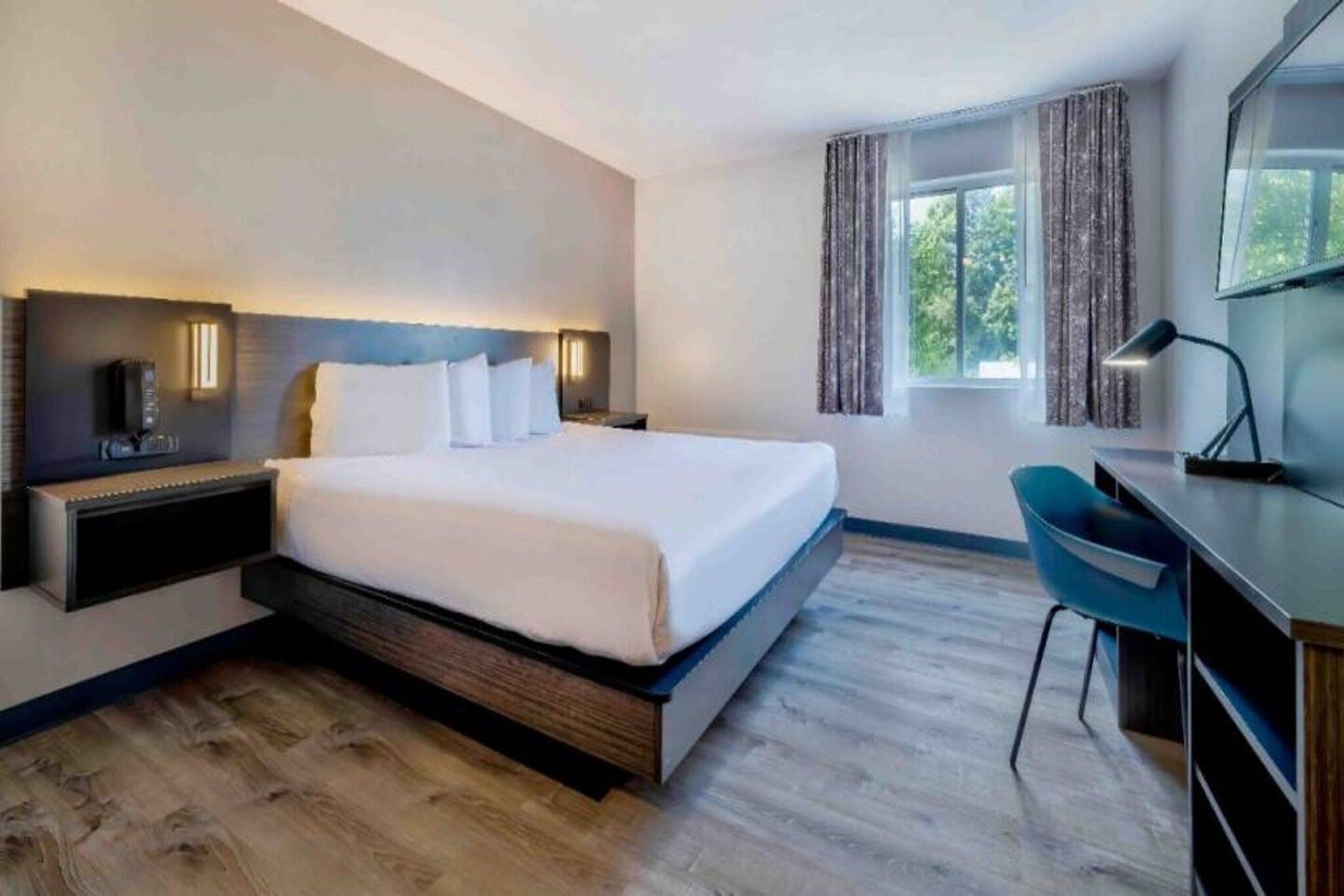A modern hotel room with a large bed, bedside tables, a desk, and a chair.