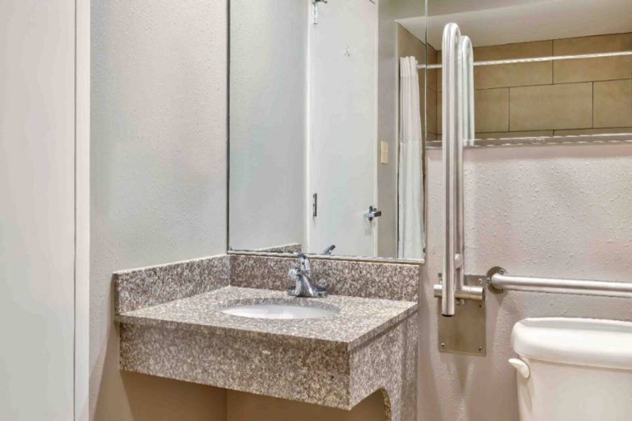 A bathroom with a granite countertop sink, a mirror, and a toilet.
