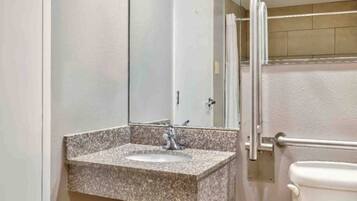 A bathroom with a granite countertop sink, a mirror, and a toilet.