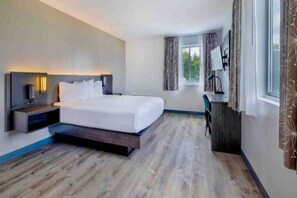 Habitación de hotel moderna con cama, mesita de noche, lámpara, escritorio y ventana.