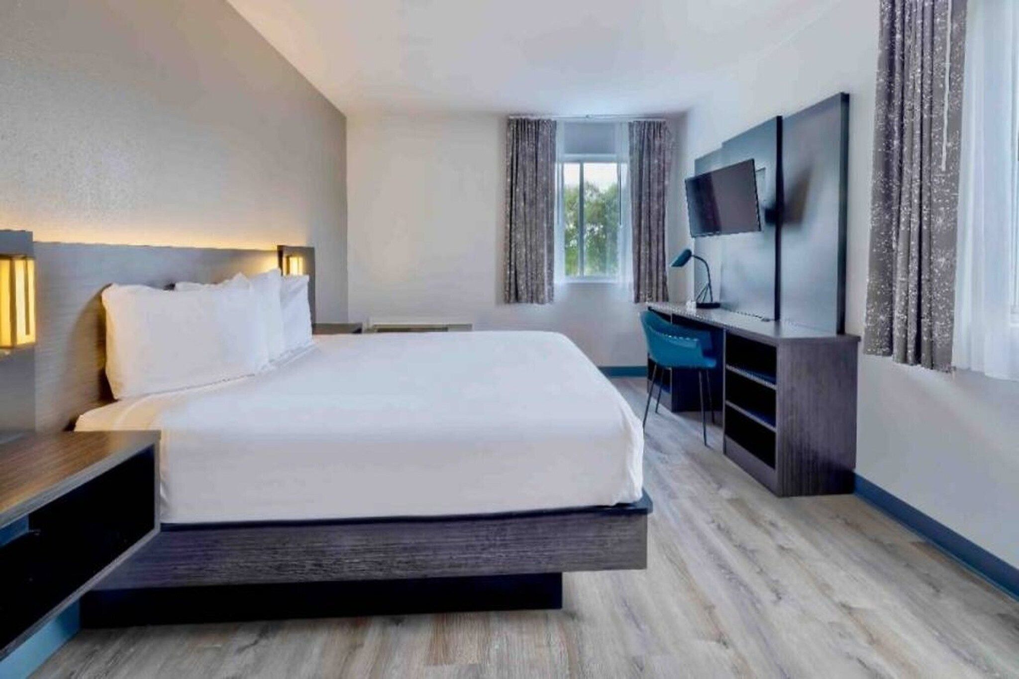 Moderni hotellihuone, jossa on suuri sänky, työpöytä, taulutelevisio ja näkymä ulos.