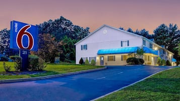 A motel with a large sign, a covered parking area, and a well-maintained lawn.