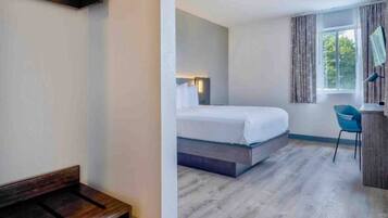 Habitación de hotel con cama, escritorio, silla y ventana.