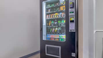 Máquina expendedora con una interfaz de pago digital y una variedad de bebidas y aperitivos.