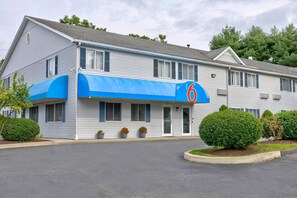 Un motel con un toldo azul, un letrero con el número 6 y un estacionamiento.