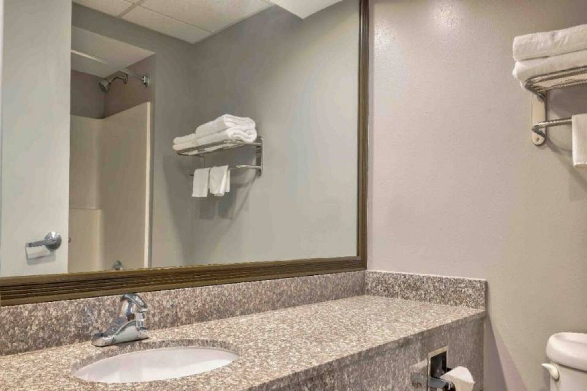 A bathroom with a granite countertop sink, a mirror, and a towel rack.