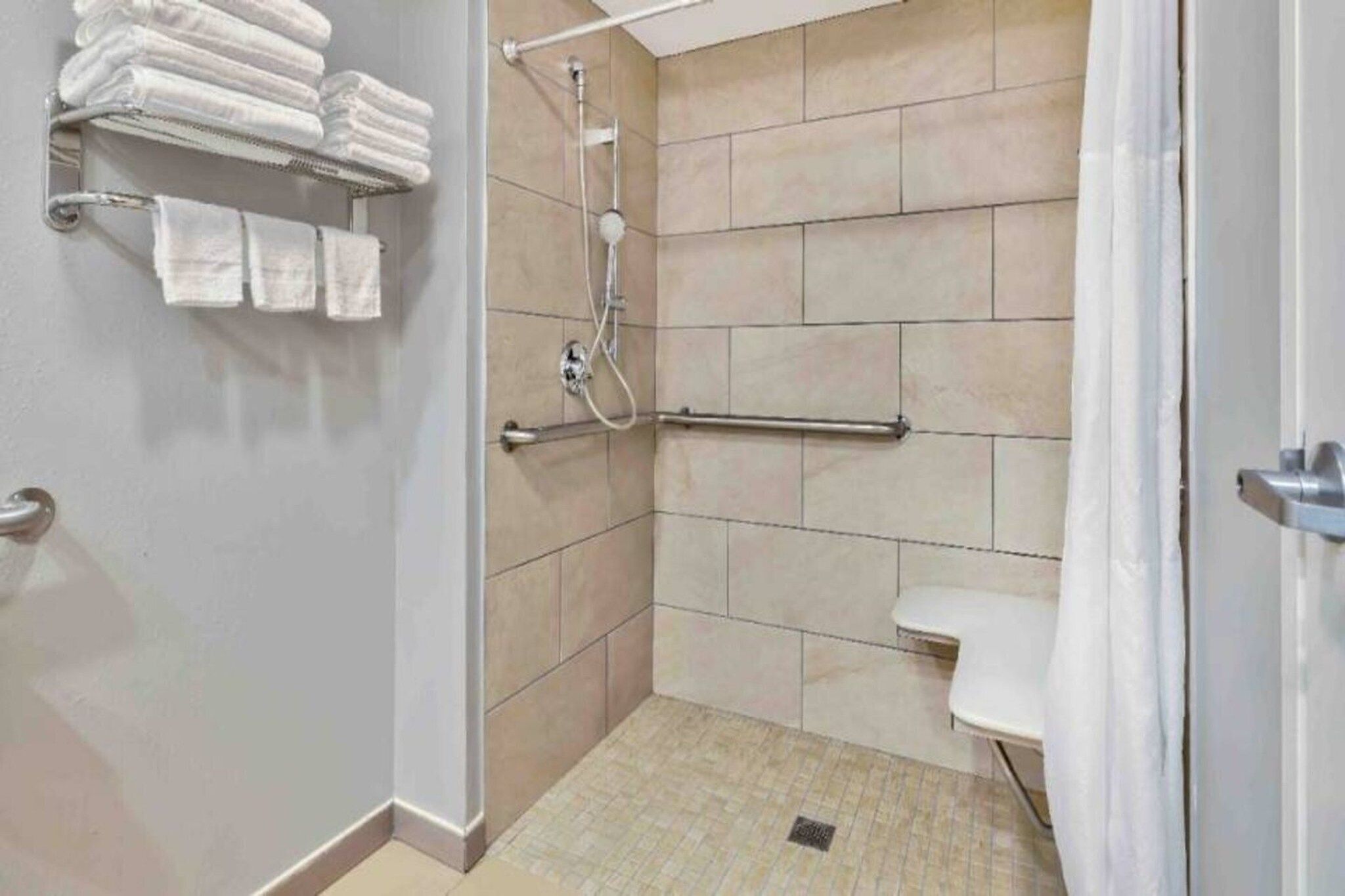 A bathroom with a shower, a toilet, and a towel rack with folded towels.