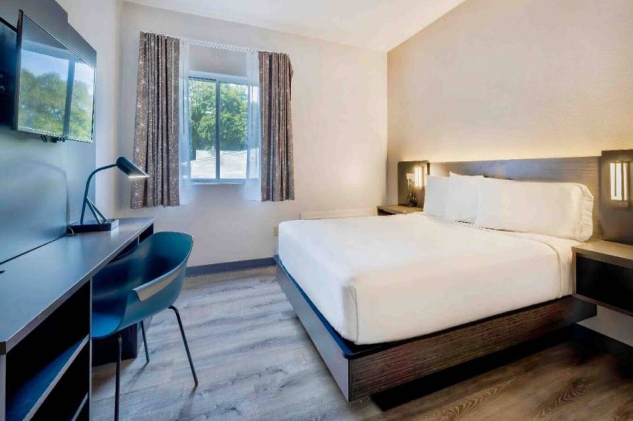 A hotel room with a bed, a desk, a chair, and a TV.