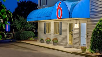 A motel with a prominent '6' sign, a covered entrance, and potted plants at the entrance.