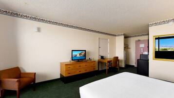 Une chambre d’hôtel comprenant un lit, un bureau, une chaise, une commode, un téléviseur et une fenêtre.