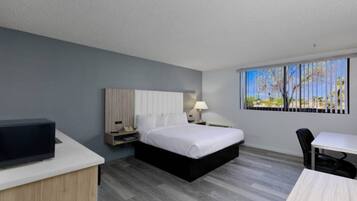 Een hotelkamer met een bed, nachtkastje, lamp, televisie, bureau, stoel en een raam met uitzicht.