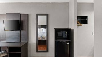 Een moderne hotelkamer met een flatscreen televisie, een ingebouwd spiegel, een minibar en een klein raam.