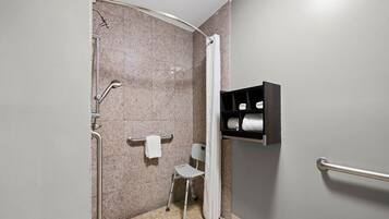 A bathroom with a shower, a grab bar, a towel rack, and a shelf with towels.