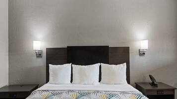 A hotel room with a bed, two bedside tables, a wall-mounted lamp, and a telephone.