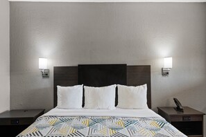 Una habitación de hotel con una cama, dos mesitas de noche, una lámpara de pared y un teléfono.