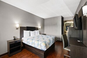Una habitación de hotel con cama, mesitas de noche, escritorio con silla, televisor y espejo.