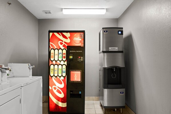 Máquina expendedora con logotipo de Coca-Cola y dispensador de agua en una habitación con piso de baldosas y un mueble blanco.