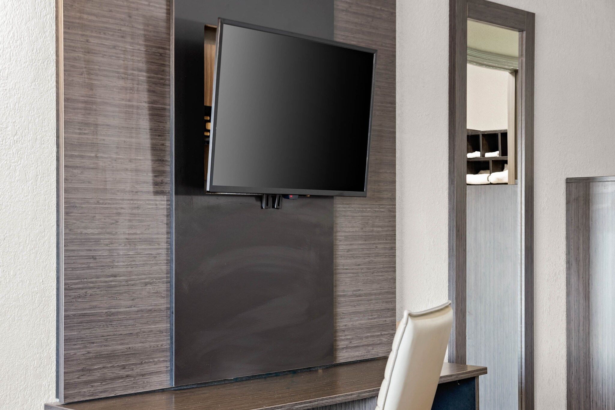 A modern room with a flat-screen TV mounted on a dark wall, a wooden cabinet below, and a white chair.