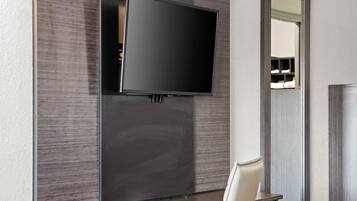 A modern room with a flat-screen TV mounted on a dark wall, a wooden cabinet below, and a white chair.