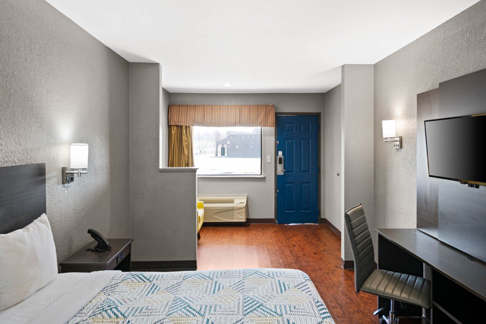 Une chambre d’hôtel comprenant un lit, un bureau, une chaise, une télévision, une fenêtre avec des rideaux et une porte.