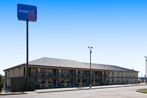 Un motel con un edificio grande de una sola planta, múltiples ventanas y un letrero llamativo que indica que es el motel número 6.
