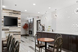 Interior moderno de restaurante con una televisión de pantalla plana montada en una pared de madera, una mesa redonda con sillas y una cafetera en la barra.