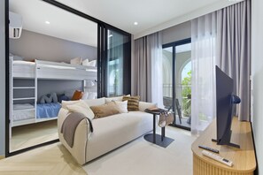 Une chambre d’hôtel moderne dotée d’un canapé, d’une télévision, d’un balcon avec des rideaux et d’une armoire intégrée avec des étagères.