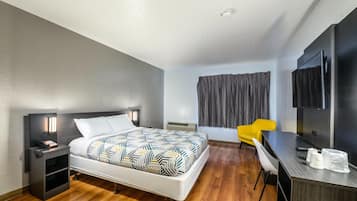 Ett modernt hotellrum med en säng, ett nattduksbord, en stol, ett skrivbord och en tv.