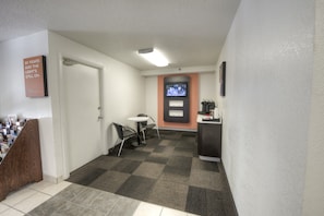 Un hall de hotel con una recepción, un televisor en la pared y una puerta que da a una habitación.