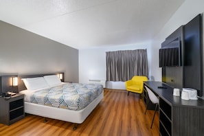 Habitación de hotel con cama, escritorio, silla, televisor y cortina.