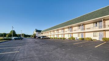 A motel with a parking lot, multiple rooms, and a green roof.