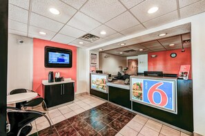 A hotel reception area with a counter, a TV mounted on the wall, a clock, and a sign indicating the room number. - Cozy 1 Queen Bed | Micfridge (East Lyme)