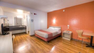 Una camera d'albergo con un letto, un comodino, una sedia e una scrivania con un computer.