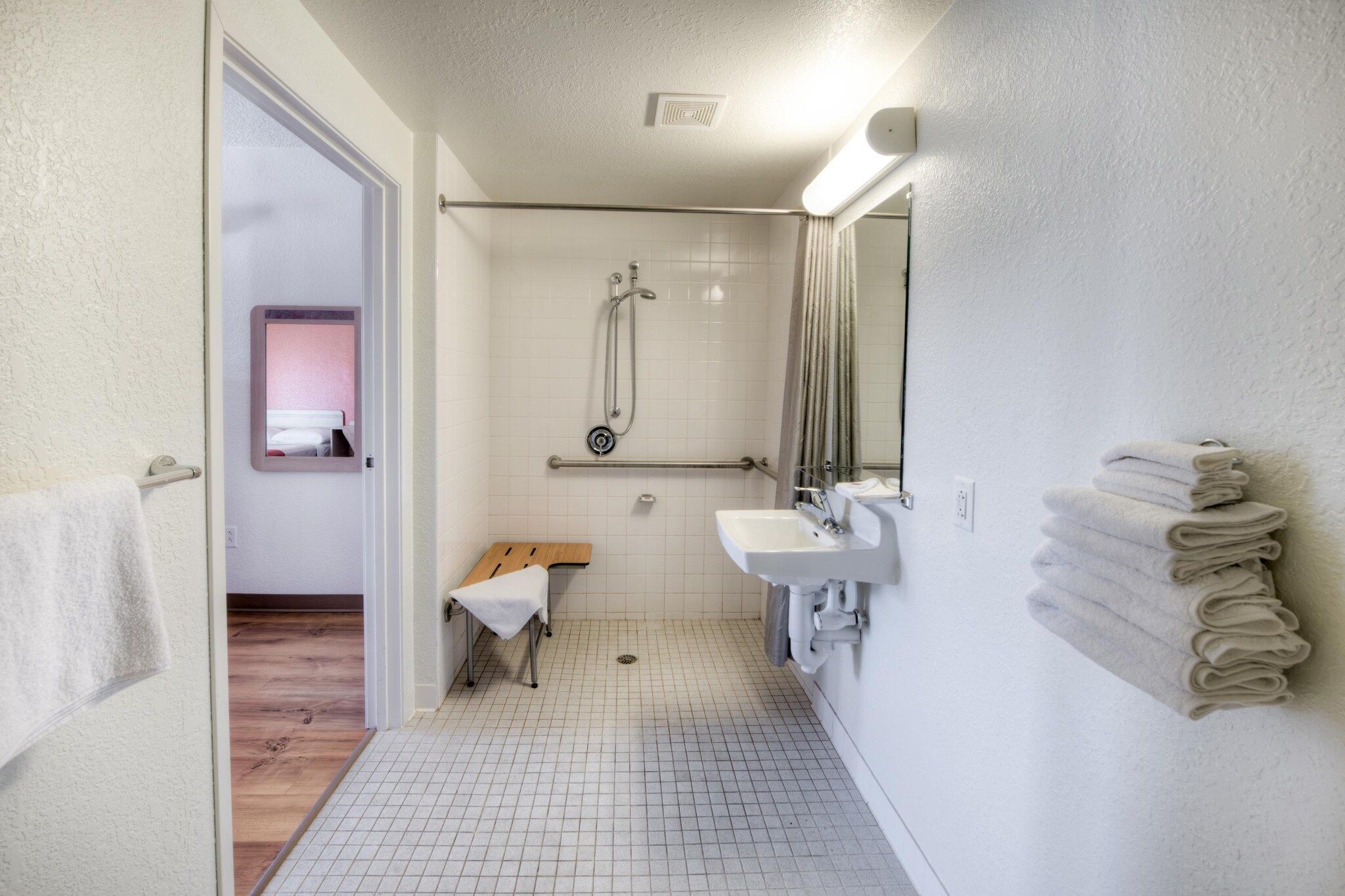 Un baño con ducha, un banco, un lavabo y un espejo.