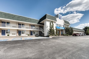 A motel with a 'Welcome' sign, parking spaces, and a clear sky.