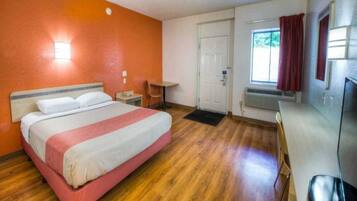 Habitación de hotel con una cama, un escritorio, una silla, una puerta y una ventana con cortinas.
