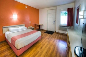 Habitación de hotel con cama, escritorio, silla, ventana con cortinas y televisor.