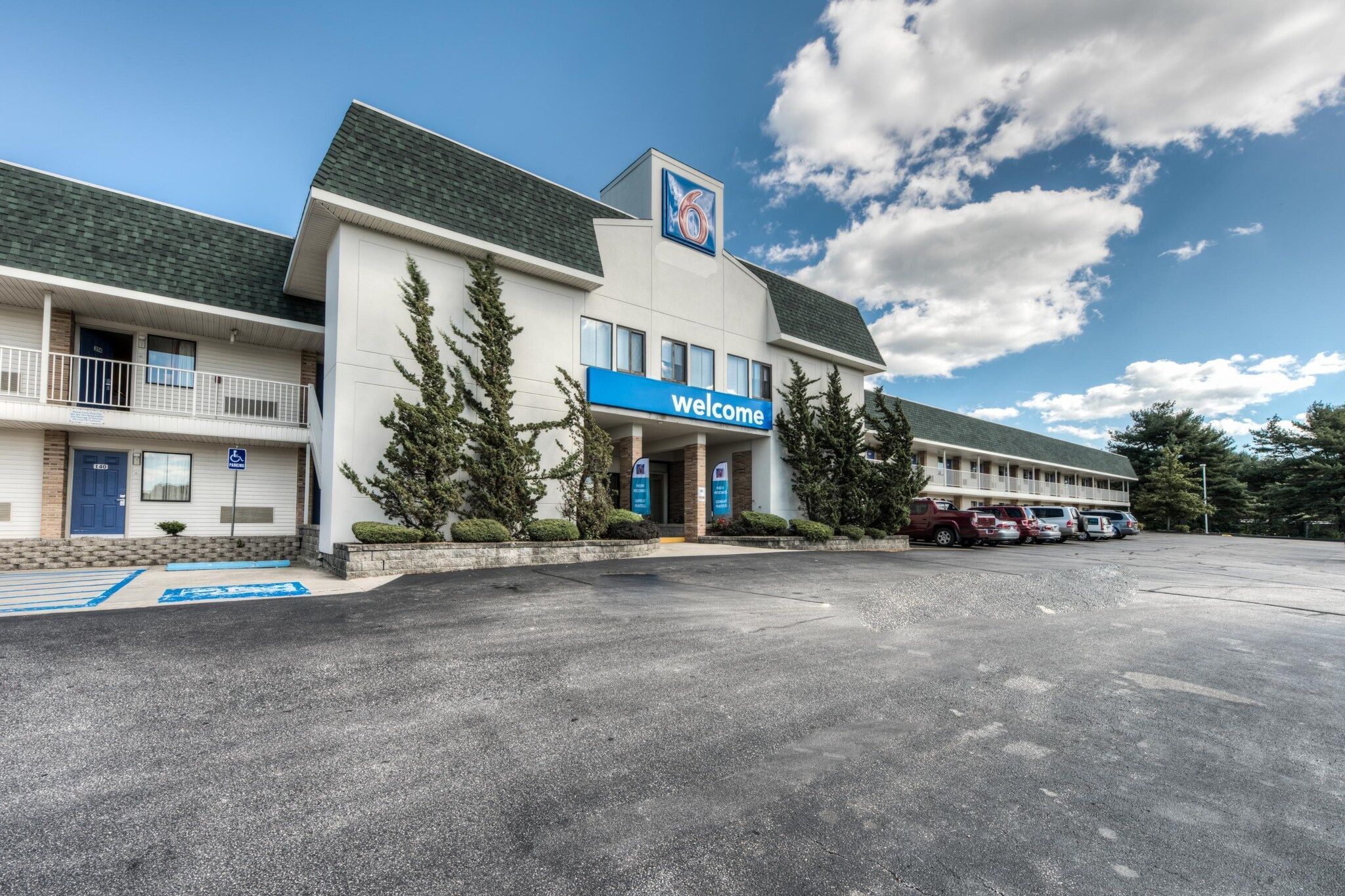 Un motel con un letrero de 'Welcome', un estacionamiento y un edificio con techo verde.