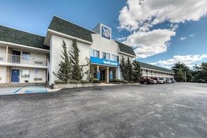 Un motel con un letrero de 'Welcome', un estacionamiento y un edificio con techo verde.