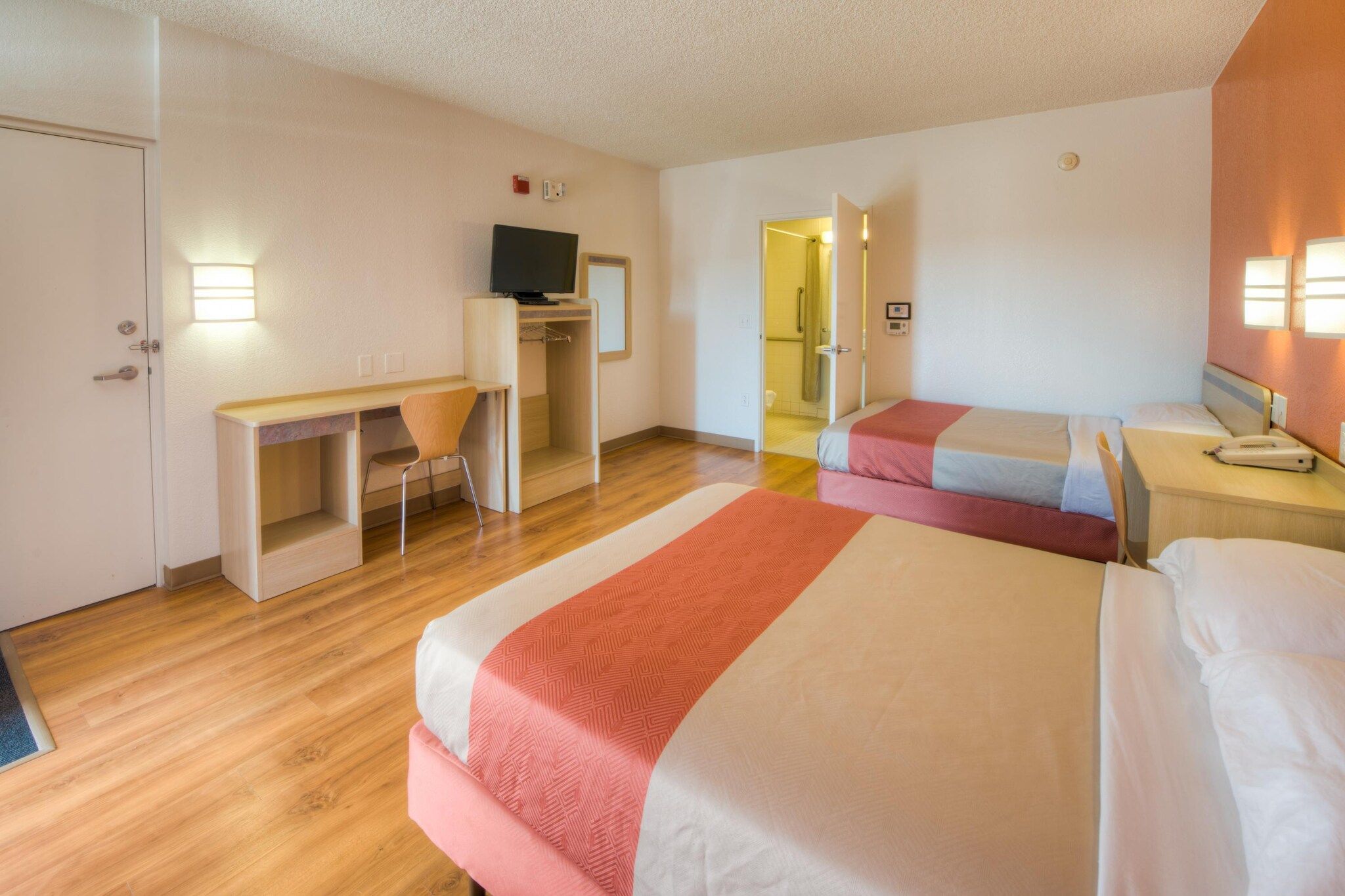 A hotel room with two beds, a desk, a chair, and a television.