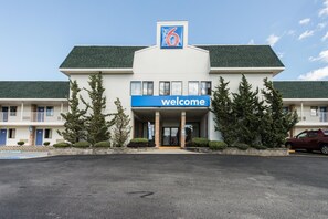 Un motel con un letrero que dice 'Welcome', un estacionamiento y un coche rojo aparcado fuera.