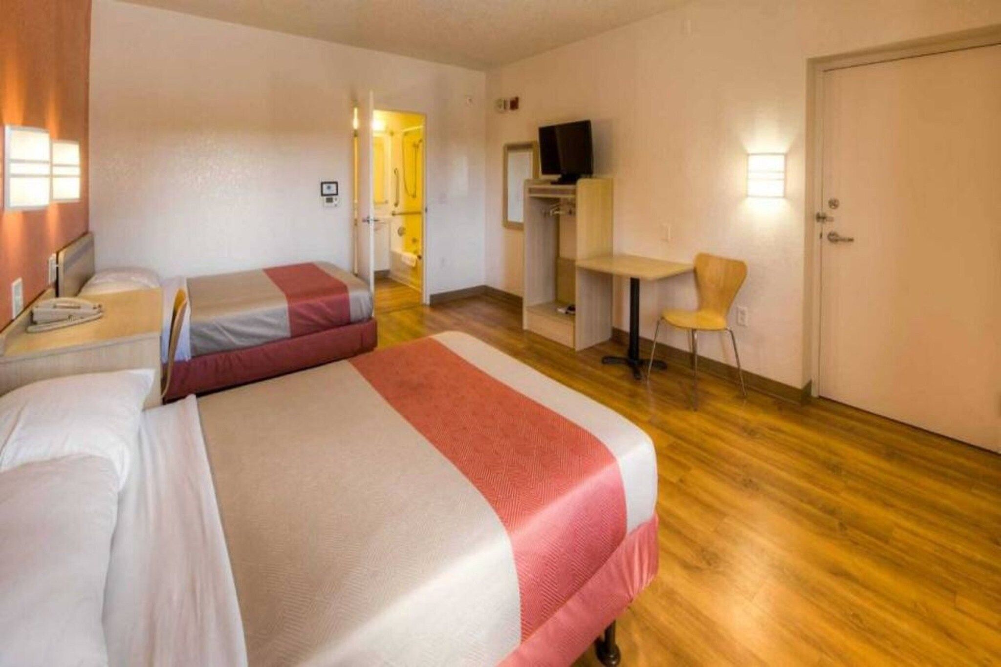A hotel room with two beds, a desk, a chair, a television, and a door.