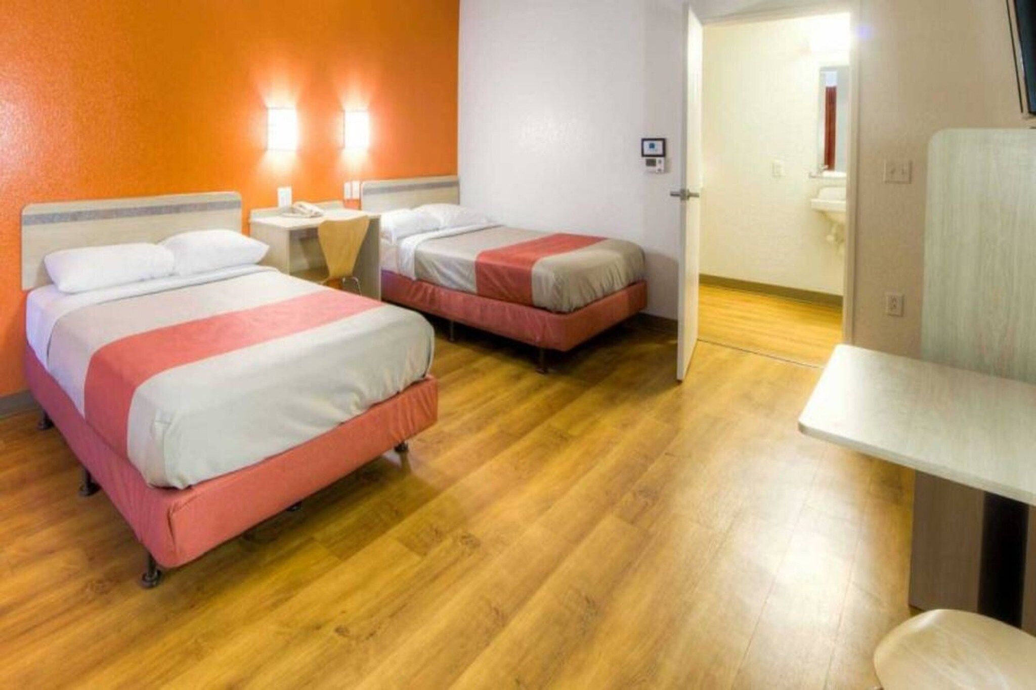 A hotel room with two beds, a small bedside table, a chair, and a bathroom visible through an open door.