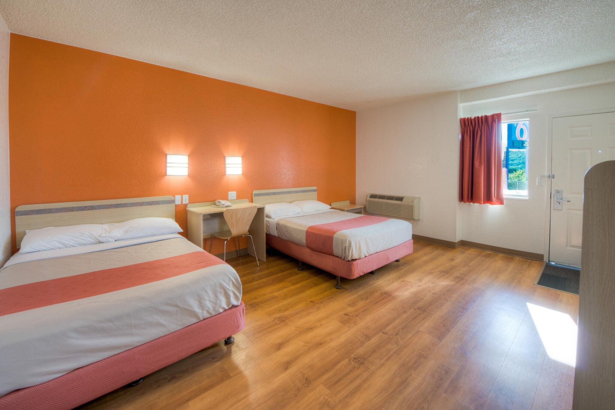 A hotel room with two beds, a desk, and a window with curtains.