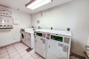 Un lavadero con varias lavadoras y secadoras, un letrero que indica el uso de detergente Tide, y una unidad de aire acondicionado montada en la pared.