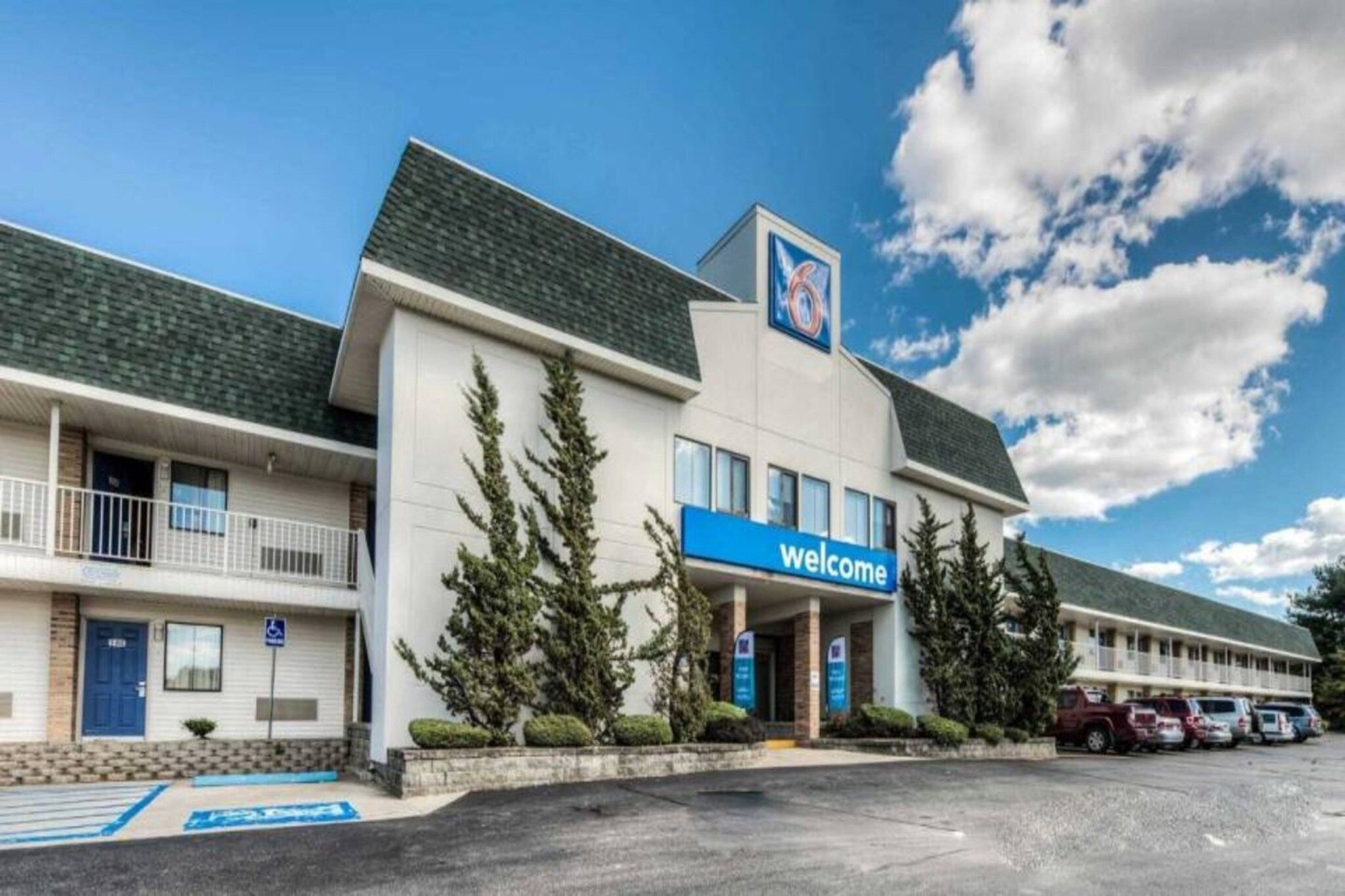 Un hotel con un letrero de 'Welcome', un estacionamiento y un cielo despejado.