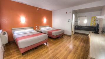 Een hotelkamer met twee bedden, een houten vloer, een badkamer met een spiegel en een bureau met een computer.