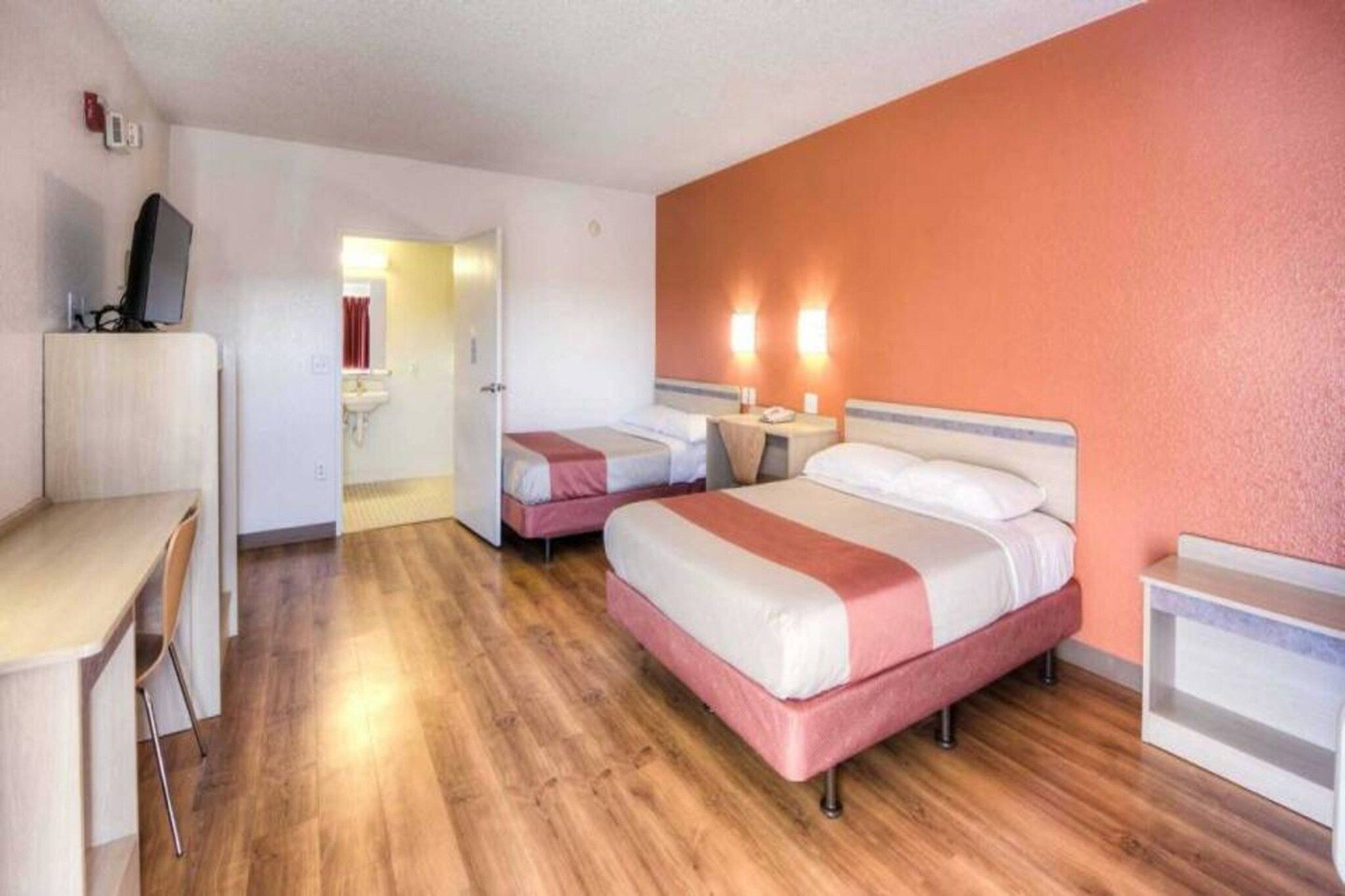 Een hotelkamer met een bureau, twee bedden, een badkamer en een televisie.